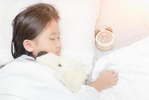 schattig weinig Aziatisch meisje slaap en knuffel pop Aan bed foto