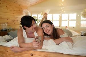 jong paar in de zolder slaapkamer in de ochtend, zeggen Hoi naar pals online gebruik makend van smartphone. foto