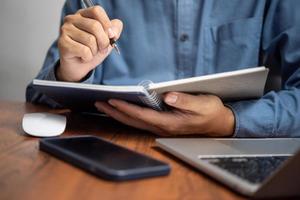 Mens Holding een pen naar schrijven logboek en dagboek van werk, studie en opleiding, Onderzoek of vind een baan Bij zijn bureau. foto