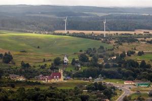 antenne panoramisch visie van groen dorp met huizen, schuren en grind weg in Woud met windmolens foto