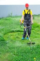 een mannetje tuinman maait de groen gras van de gazon in de achtertuin met een benzine maaier. trimmer voor de zorg van een tuin verhaal foto