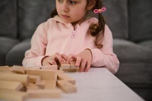 focus Aan de handen van een schattig baby meisje, Aan houten blokken, terwijl ze spelen ontwikkelingsstoornissen en leerzaam bord spel, gebouw structuren van bakstenen. prima motor vaardigheden ontwikkeling concept foto