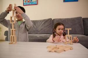 aanbiddelijk geconcentreerd Kaukasisch kinderen zittend Bij tafel en spelen bord spel, gebouw toren met houten blokken. prima vaardigheid motoren ontwikkeling, leerzaam spellen, vrije tijd, familie verhouding concept foto