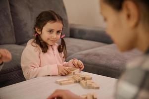 schattig baby meisje in roze sweater spelen bord spel, gebouw houten structuren met blokken, glimlacht op zoek Bij haar mama. familie tijdverdrijf, leerzaam vrije tijd en prima motor vaardigheden ontwikkeling concept foto