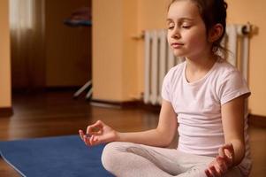 vredig weinig kind meisje Holding vingers in mudra gebaar, mediteren met haar ogen Gesloten. yoga praktijk en meditatie foto
