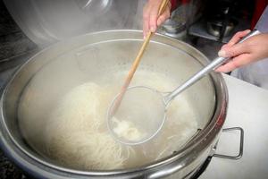 chef is scheppen gekookt noedels in koken water in pot foto