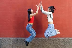 blij jong Aziatisch vriendinnetjes geven hoog vijf terwijl jumping foto