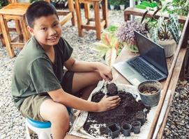 jongen leert naar toenemen bloemen in potten door online onderwijs. scheppen bodem in potten naar bereiden planten voor aanplant vrije tijd activiteiten concept foto