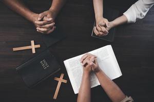 klein groepen van christenen houden handen en bidden samen in de omgeving van een houten tafel met Bijbel Pagina's en kruisen. Bijbel studie groep aan het leren religieus concepten in de Bijbel. aanbidden god. foto