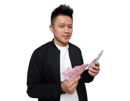 knap Mens Holding smartphone en Holding Indonesisch geld glimlachen op zoek Bij camera foto
