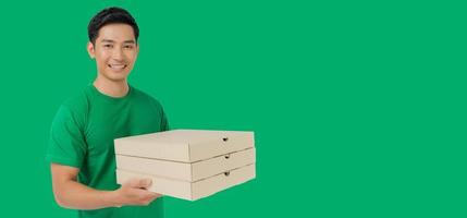 de glimlachen pizza levering Mens staat Aan een groen achtergrond Holding de pizza doos en vervelend een groen t-shirt uniform. foto