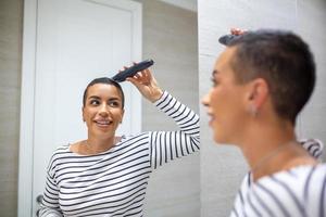 spiegel reflectie van kort haren vrouw in tank top gebruik makend van haar knippen machine foto