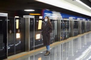een vrouw met een medisch gezichtsmasker wacht in de metro op een aankomende trein