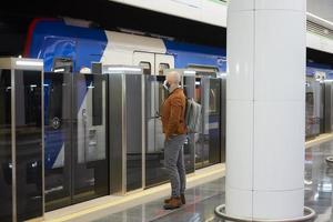 een man met een gezichtsmasker houdt een smartphone vast terwijl hij op een metro wacht foto