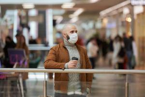 een man met een gezichtsmasker houdt een kopje koffie vast in het winkelcentrum