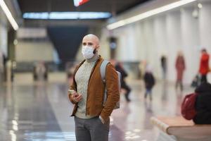 een man met een gezichtsmasker gebruikt een smartphone terwijl hij op een metro wacht