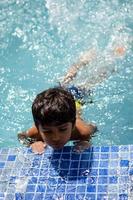 gelukkig Indisch jongen zwemmen in een zwembad, kind vervelend zwemmen kostuum langs met lucht buis gedurende heet zomer vakanties, kinderen jongen in groot zwemmen zwembad. foto