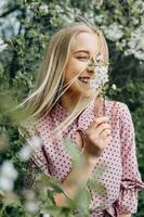 blond meisje Aan een voorjaar wandelen in de tuin met kers bloeit. vrouw portret, detailopname. een meisje in een roze polka punt jurk. foto