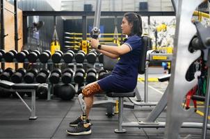 jong vrouw met een prothetisch been met schouder opdrachten met oefening machines naar trein de spieren in de torso en schouders, de concept van leven een vrouw leven met een prothetisch been. foto