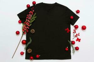 dichtbij omhoog zwart blanco sjabloon t overhemd met kopiëren ruimte en Kerstmis vakantie concept. top visie mockup t-shirt en rood vakantie decoraties Aan wit achtergrond. gelukkig nieuw jaar accessoires. Kerstmis kleding foto