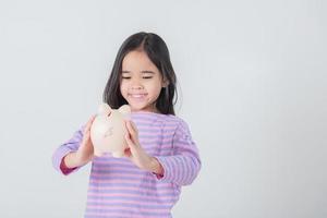 klein Aziatisch meisje dat geld spaart in een spaarvarken, leert over sparen, kind spaart geld voor toekomstig onderwijs. geld, financiën, verzekeringen en mensenconcept foto