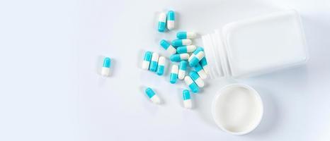 blauwe en witte capsules pillen gieten uit de fles op witte achtergrond foto