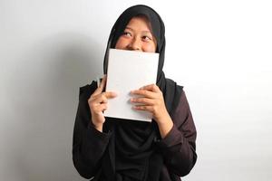 gelukkig jong Aziatisch meisje aan het bedekken haar gezicht met boek Aan wit achtergrond foto
