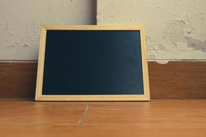 een klein zwart schoolbord met een houten kader rust Aan een houten getextureerde vloer. foto