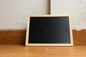 een klein zwart schoolbord met een houten kader rust Aan een houten getextureerde vloer. foto