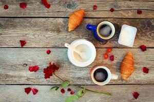 twee koffie, croissants, suiker, snoep, yoghurt, roos en bloemblaadjes Aan oud houten achtergrond. top visie. foto