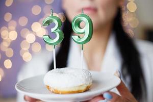 vrouw Holding een taart met de aantal 39 kaarsen Aan feestelijk wazig bokeh achtergrond foto