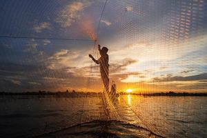 silhouet van visser op vissersboot met net op het meer bij zonsondergang, thailand foto