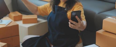 opstarten mkb klein bedrijf ondernemer van freelance Aziatisch vrouw vervelend schort gebruik makend van laptop en doos naar te ontvangen en recensie bestellingen online naar bereiden naar pak verkopen naar klanten, online mkb bedrijf ideeën. foto