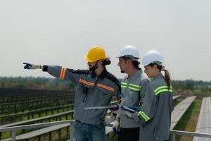 Aan de op het dak van een groot zonne- energie opslagruimte station gebouw een team van elektrisch macht ingenieurs inspecteren zonne- panelen dat hebben geweest geïnstalleerd Aan honderden van hectare van velden. foto