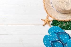 rietje hoed, groen blad, blauw omdraaien flops en zeester Aan een wit houten achtergrond. top visie zomer vakantie concept met kopiëren ruimte foto