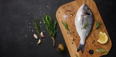 rauw geheel dorado vis Aan houten keuken bord en specerijen voor Koken, top visie Aan zwart tafel foto