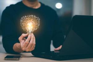 zakenman hand- Holding licht lamp met pictogrammen en werken Aan de bureau, creativiteit en innovatie zijn sleutels naar succes.concept van nieuw idee en innovatie met energie en macht , werken Bij huis, foto