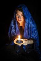 trieste jonge vrouw met kaars en blauwe hoofddoek foto