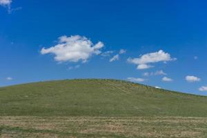groene heuvel bedekt met gras tegen een blauwe hemel met wolken.