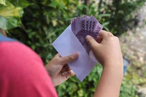 dichtbij omhoog van mannetje hand- invoegen tien duizend roepia geld bankbiljet in envelop. financieel en spaargeld concept foto