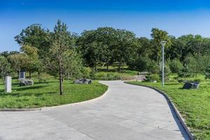 een pad in een modern, goed onderhouden park met groene bomen en een houten brug foto