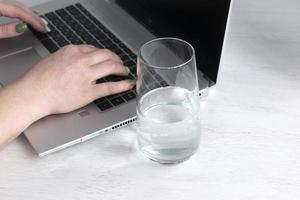vrouw werken met laptop terwijl drinken glas van water Aan een tafel Bij huis. foto
