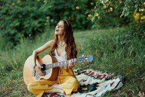 jong vrouw hippie artiest Toneelstukken gitaar en zingt liedjes in milieuvriendelijk kleding zittend Aan de grond buiten in natuur in de herfst op zoek uit Bij de zonsondergang foto