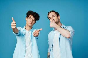 jong jongens in de dezelfde overhemden en t-shirts zijn gebaren met hun handen Aan een blauw achtergrond vrienden foto