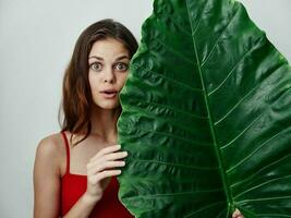 vrouw in een rood zwempak groot groen blad in haar handen verrast kijken detailopname foto