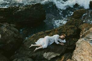 mooi jong vrouw aan het liegen Aan rotsachtig kust met scheuren Aan rotsachtig oppervlakte landschap foto