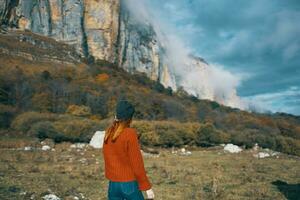 een vrouw in een trui houdt haar handen achter haar hoofd en looks Bij de hoog bergen landschap blauw lucht wolken foto