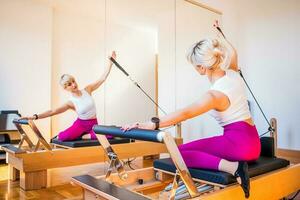 blond vrouw is oefenen Aan pilates hervormer bed in haar huis. foto