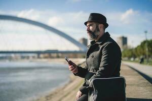 Mens is zittend buitenshuis in de stad en gebruik makend van de telefoon. foto