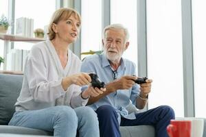 gelukkig senior stel, ouderen familie, hand- van blanken volwassen, volwassen minnaar en gepensioneerd echtgenoot, vrouw hebben plezier, spelen video spel samen, zittend knus Aan sofa in leven kamer Bij huis, technologie. foto